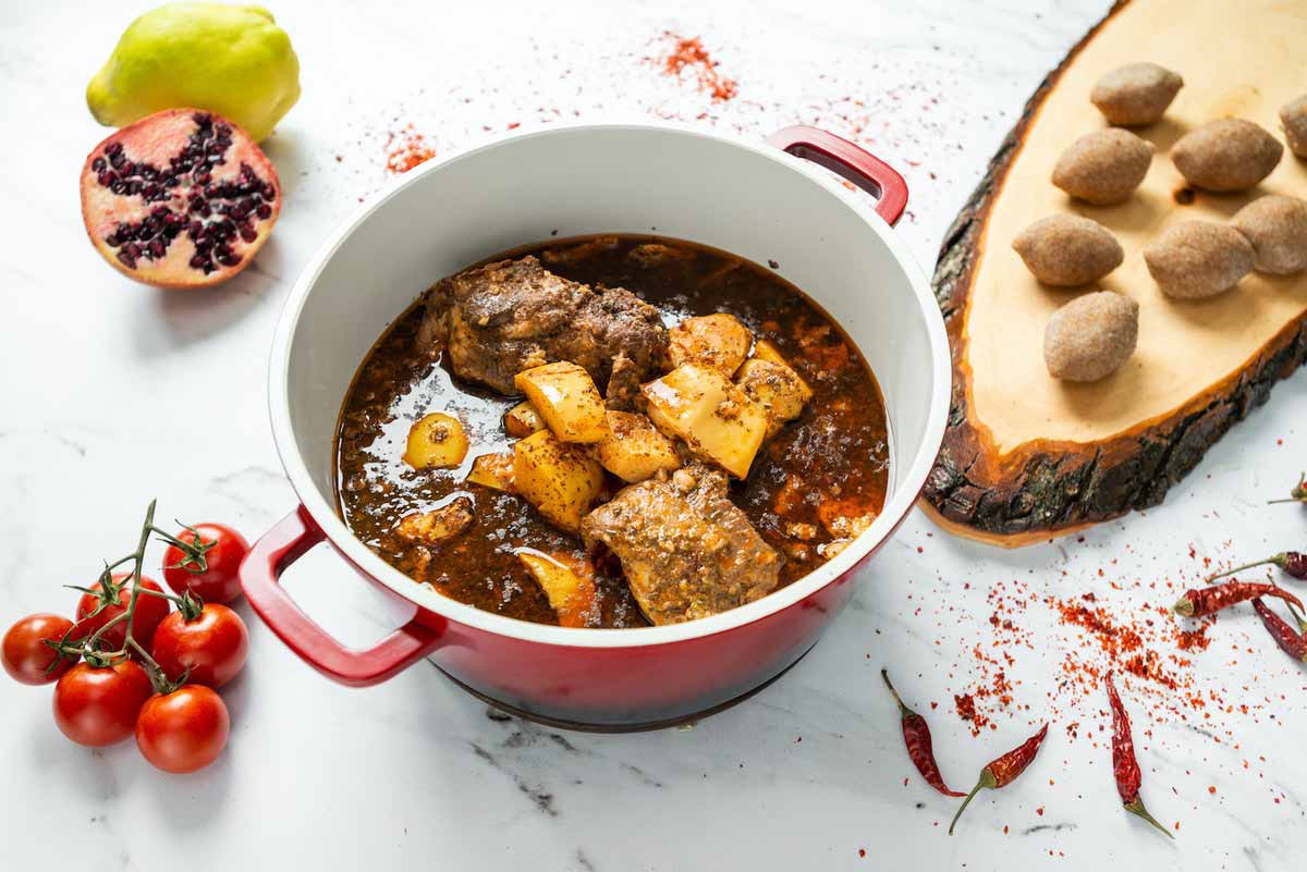 Catering Berlin Quitten-Eintopf mit Fleisch in einem roten Topf, serviert mit Reis oder Kibbeh auf einem Holzbrett.
